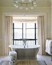 a beige and creamy bathroom with a large window that brigns much natural light inside