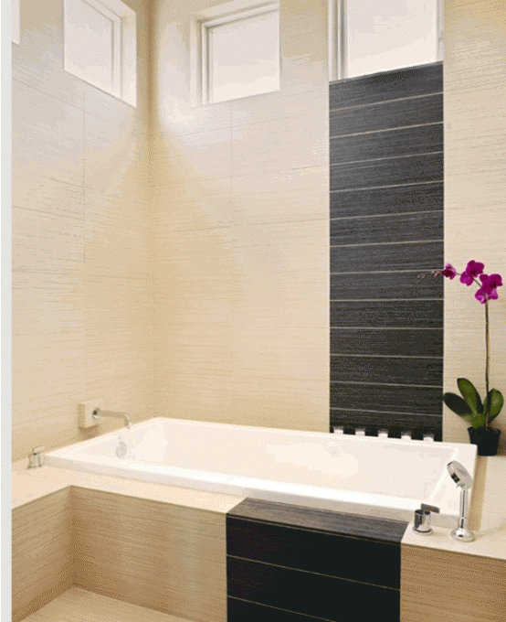 a beige bathroom spruced up with dark tiles and a white bathtub is a chic space