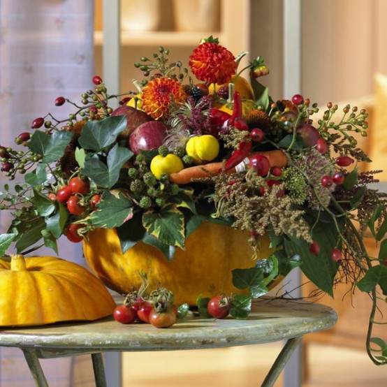 a super bold and all-natural Thanksgiving centerpiece with a bold pumpkin as a vase, lots of fresh veggies, berries, greenery and some brigth blooms is gorgeous