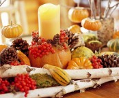a rustic Thanksgiving centerpiece with pinecones, berries, gourds and pumpkins, moss and candles is a quirky and catchy solution