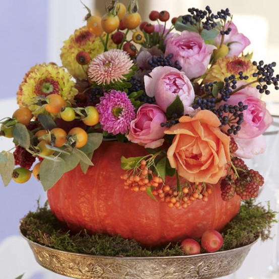 a bright Thanksgiving centerpiece of a pumpkin as a vase, pink, coral and yellow blooms and greenery and some berries