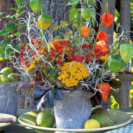 a bold rustic Thanksgiving centerpiece of a bucket, bold blooms, greenery and dried flowers  and some fresh apples right on the plate