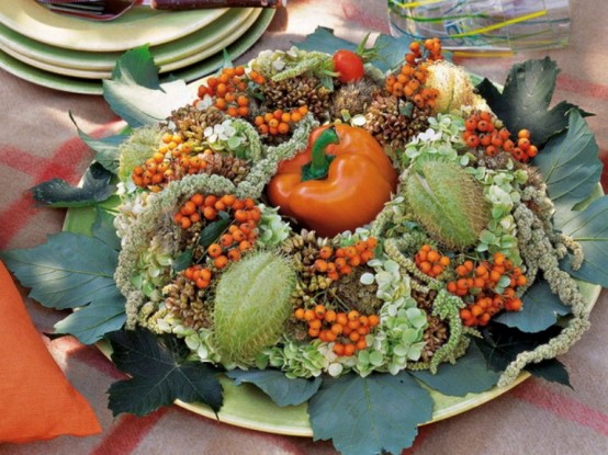 a pretty Thanksgiving centerpiece of a plate with greenery, berries, fruits and an orange pepper in the center is a creative all-natural idea