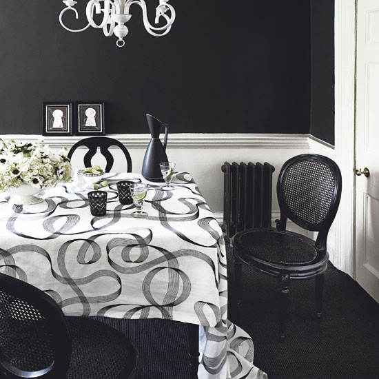 a black and white dining room with black walls, white paneling, a table with a black and white tablecloth, black chairs and a crystal chandelier