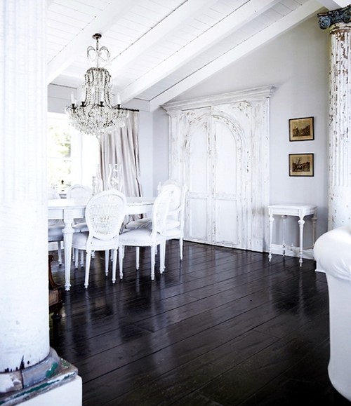 a vintage dining space with whitewashed walls and a ceiling, a black floor and a white dinign set, a crystal chandelier