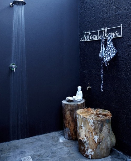 an outdoor black bathroom with black walls, a shower, tree stumps and a rack is a cool idea for a Nordic or modern outdoor space