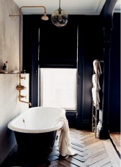 a vintage bathroom with limewashed walls, a black clawfoot bathtub, a black accent wall and a black curtain, brass fixtures is a lovely space to be in