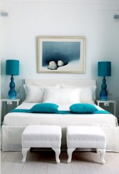 a beautiful ocean bedroom done in neutrals and spruced up with turquoise and blues, a white bed and stools, turquoise lamps and pillows and artwork