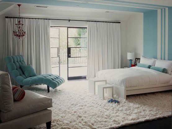 a peaceful neutral bedroom with light blue and turquoise accents, blue stripes on the wall and ceiling, a white bed and bedding, a turquoise lounger and a chic chandelier