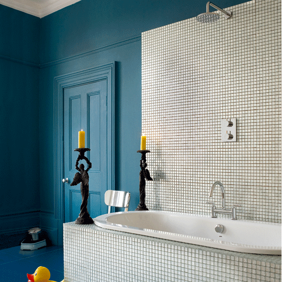 blue painted walls and a neutral tile clad bathtub with a backsplash and candles for a refined feel