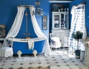 a bright blue bathroom with a bold clawfoot bathtub and white furniture and textiles