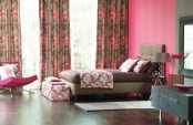 a pink bedroom with colorful printed curtains, a taupe upholstered bed with bright bedding and a printed bench, a fuchsia chair and a black vanity is super bold and catchy