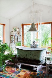 a boho vintage bathroom with colorful tiles, a shabby chic bathtub, lots of potted greenery and a gallery wall