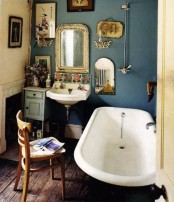 a vintage bathroom with blue walls, a free-standing tub, a gallery wall and artworks plus vintage furniture