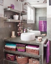 a grey bathroom clad with sotne-like tiles and with bright towels and other textiles