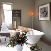 a clean bathroom with grey walls, a chic clawfoot tub, white towels and a gorgeous mirror in a unique frame