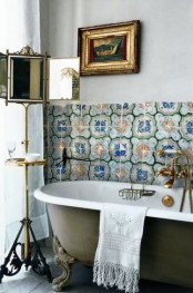 a chic bathroom with bright Moroccan tiles, a grene clawfoot tub, artworks and a fantastic mirror on a stand