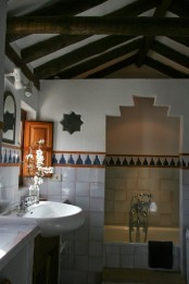 a Moroccan-inspired bathroom with a cutout shower space, Moroccan tiles and wooden beams and a white sink