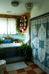 a relaxed boho bathroom with a boho blanket on the wall, a metal clad tub, potted greenery and blooms and checked tiles