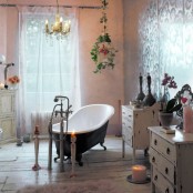 a romantic vintage and shabby chic bathroom with shabby dressers, a vintage clawfoot tub, candles, a cage and a crystal chandelier