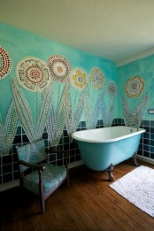 a creative bathroom with turquoise walls done with mosaic florals for a free-spirited feel, a bright clawfoot tub and a vintage chair