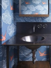 a bathroom done with blue wallpaper and coral birds, a stained vanity and a dark metal sink