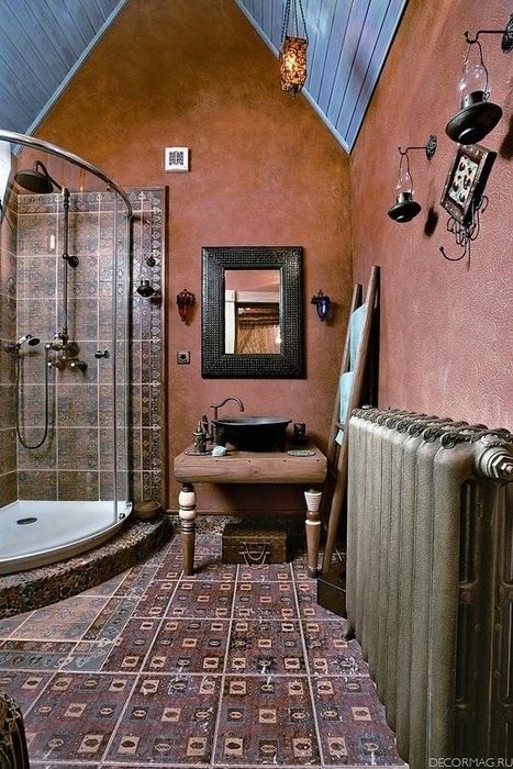 a boho meets vintage bathroom with red plaster walls, dark Moroccan tiles on the floor and in the shower, candle lanterns and an ornate mirror