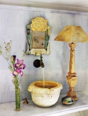 a unique bathing space with a stone carved sink, an ornate mirror, a chic lamp and a floral arrangement