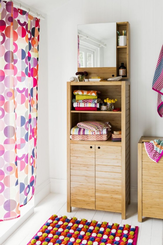 a neutral bathroom with light wooden furniture, a colorful curtain and a rug plus bright towels