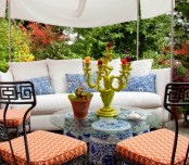 a colorful spring terrace with forged furniture, white and blue textiles and coral chairs, a tent over the space and blooms