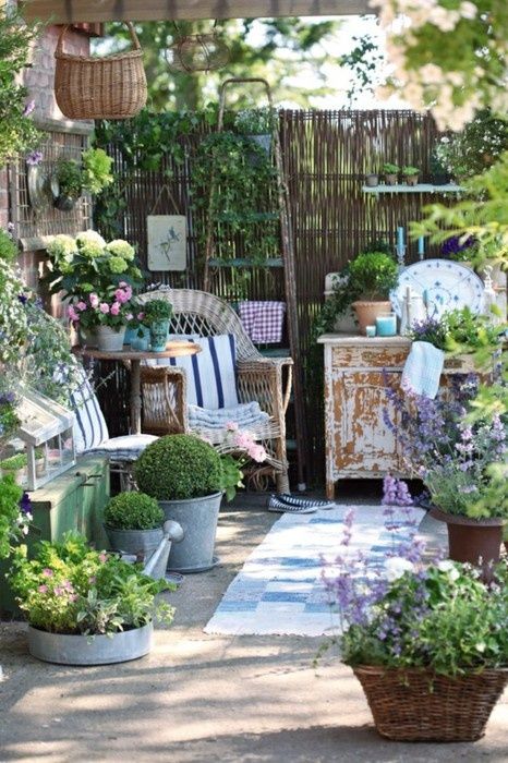 a shabby chic and rustic spring terrace with wicker chairs, shabby cabinets, baskets and buckets with greenery and blooms and decorative plates