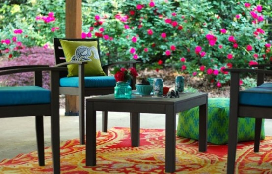 a bright spring terrace with dark furniture, colorful upholstery, bright pillows and rugs and blooms around