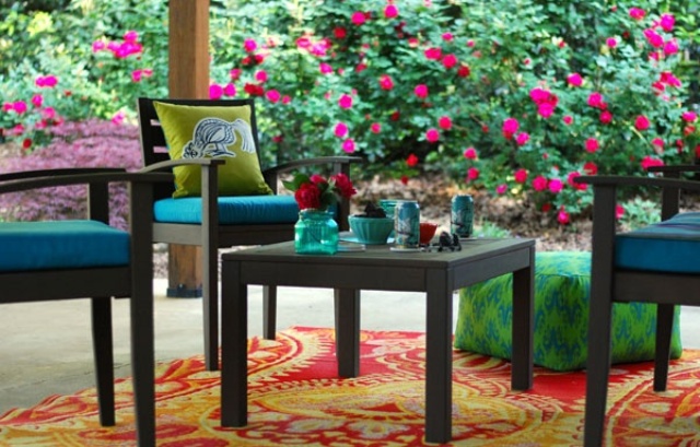 a bright spring terrace with dark furniture, colorful upholstery, bright pillows and rugs and blooms around
