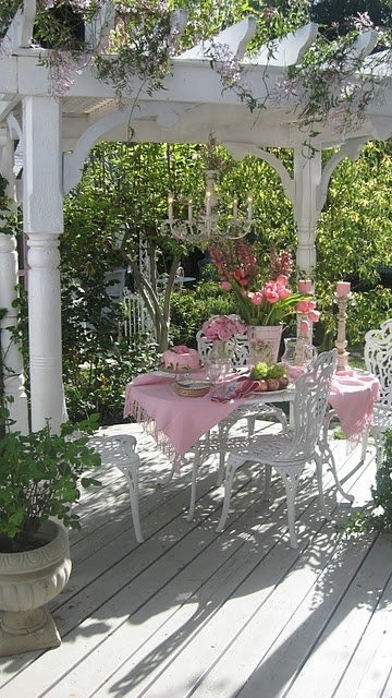 a refined vintage spring terrace with luxurious white furniture, some blooms and greenery around and pink linens is all chic