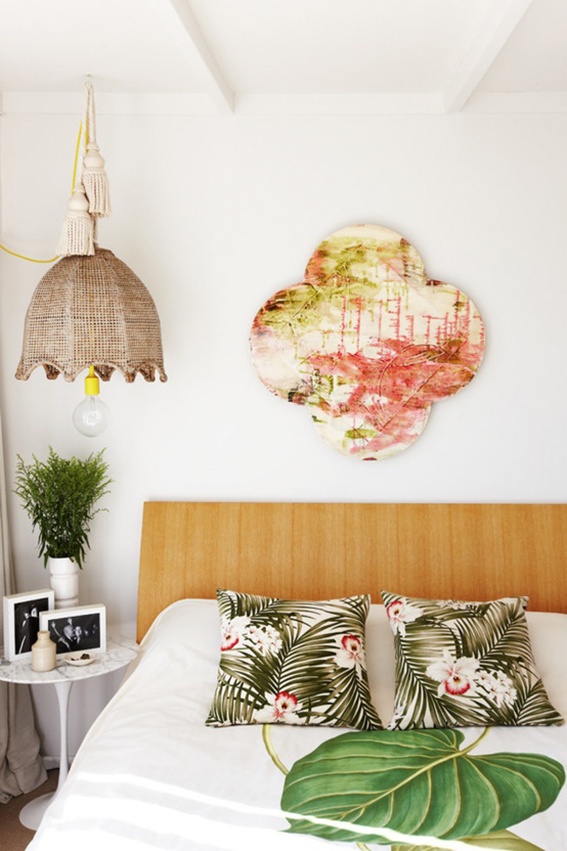a contemporary tropical bedroom with bright printed pillows, a bold artwork and a wicker lampshade over the bed