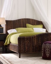a dark wicker bed with an airy sheer canopy, dark stained furniture and a purple ottoman