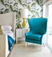 tropical print wallpaper, a bright turquoise chair and a neutral upholstered bed for a glam tropical space