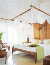 a tropical bedroom with a canopy hanging over the bed, wicker chairs, touches of green for refreshing the space