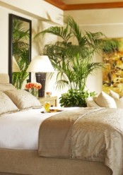 a tropical feel is achieved with potted plants and bamboo base lamps in a neutral bedroom