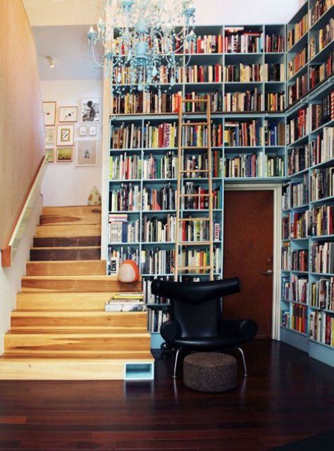 an entryway library covered with built-in bookshelves, with a vintage chandelier and a black chair is amazing to make use of your space