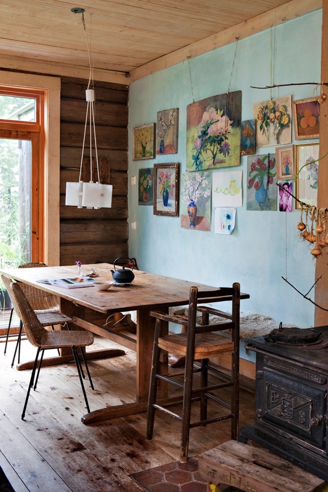 a rustic meets boho dining room with a blue accent wall with a gallery wall, a wooden table, mismatching wooden and woven chairs and a pendant lamp