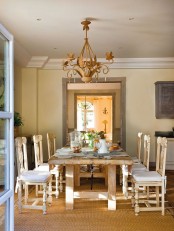 a warm-colored vintage rustic dining room with a stained dining table and stained chairs, a vintage chandelier, a large warm-colored rug for more coziness in the space