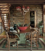 a rustic chalet dining room with a dark-stained round table, matching chairs, a red lampshade chandelier and a bowl with pinecones and evergreens