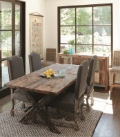 a rustic dining room with a stained trestle table, taupe wooden chairs, a reclaimed wood sideboard and woven tall stools plus a garden view