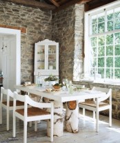 a rustic meets vintage dining room with stone walls, a white table on tree stumps, elegant white chairs and a corner buffet with a vintage elegant touch