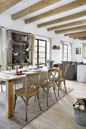 a rustic dining space with an open storage unit, a light-stained table and matching chairs, wooden beams on the ceiling, a metal shade chandelier