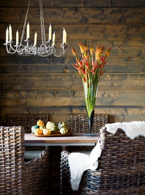 a rustic dining room with stained wood walls, a stained table and wicker chairs, a chic vintage chandelier with candles
