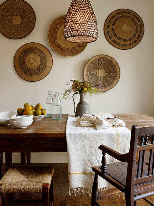 a rustic meets boho dining room with a stained dining table and chairs, a woven pendant lamp and a gallery wlal of woven plates is a lovely space for meals
