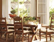 a beautiful dining space with elegant wooden furniture with white upholstery, elegant crystal chandeliers over the table and a garden view