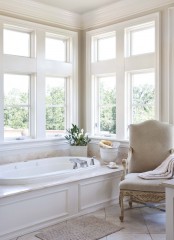 a neutral refined bathroom with a tub clad with panels, a refined vintage chair and  some blooms is a very beautiful and peaceful idea
